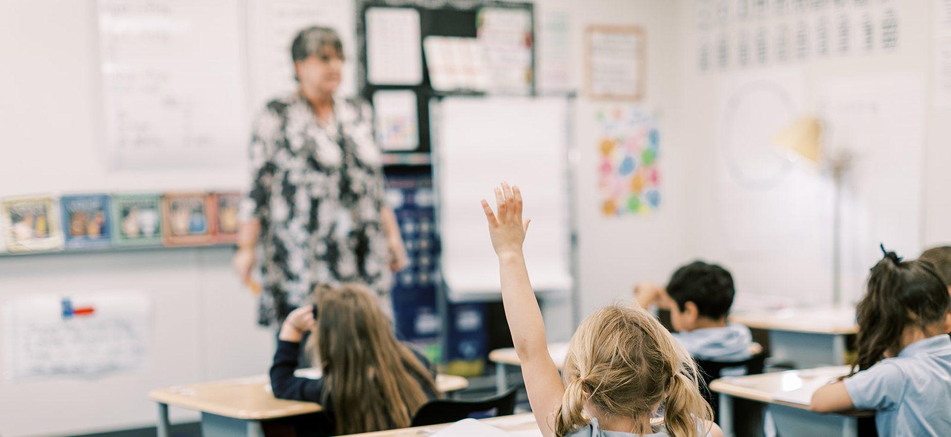 An elementary student raises her hand to answer a question in class at Founders Classical Academy of Bastrop