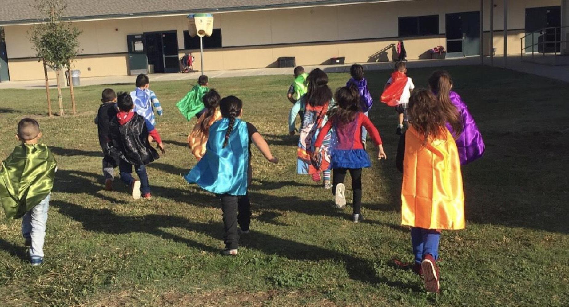 Students dressed as superheroes running across the grass.