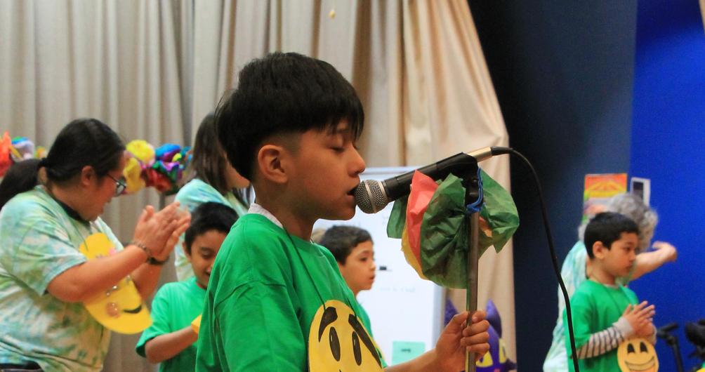 Children in green shirts performing with smiley face props on stage.