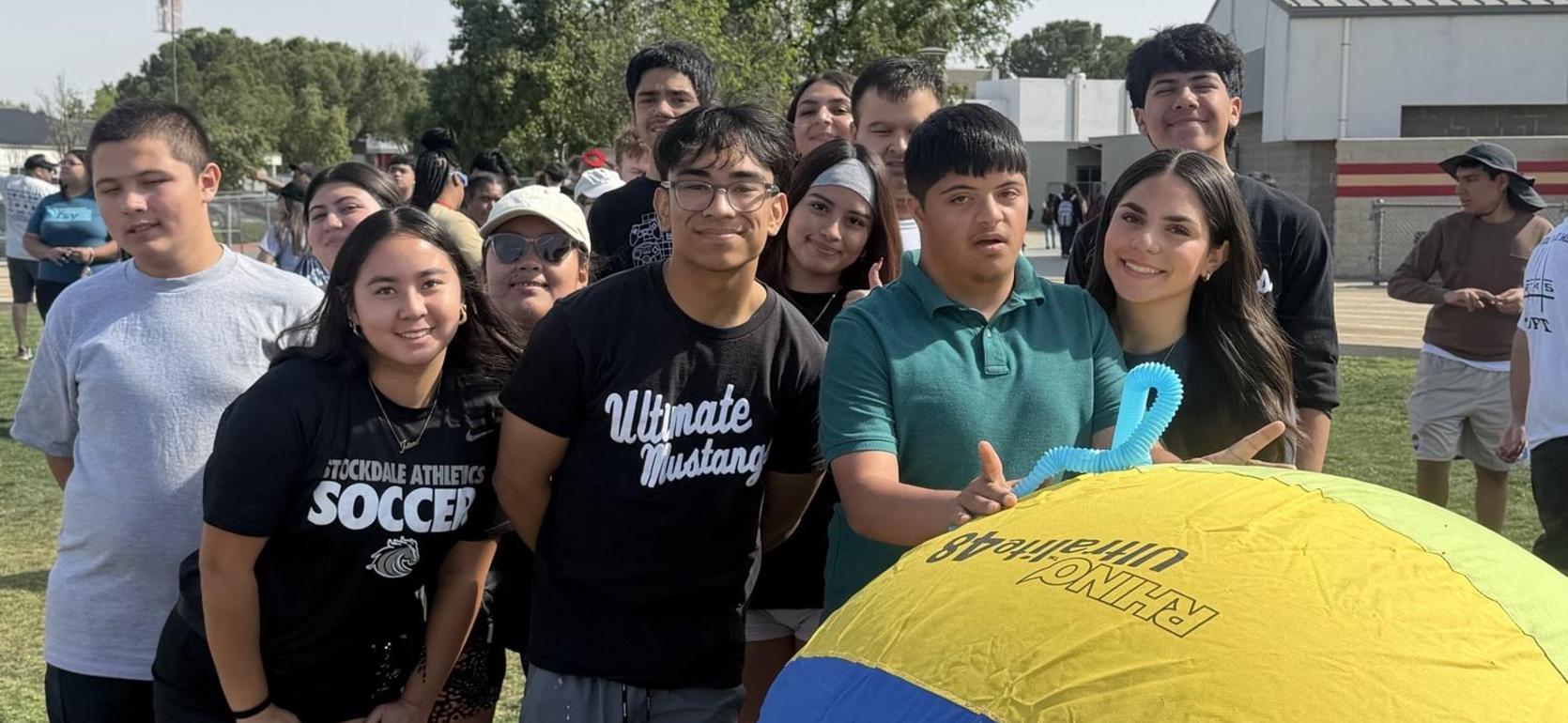 Group of students gathered around a colorful beach ball outdoors.