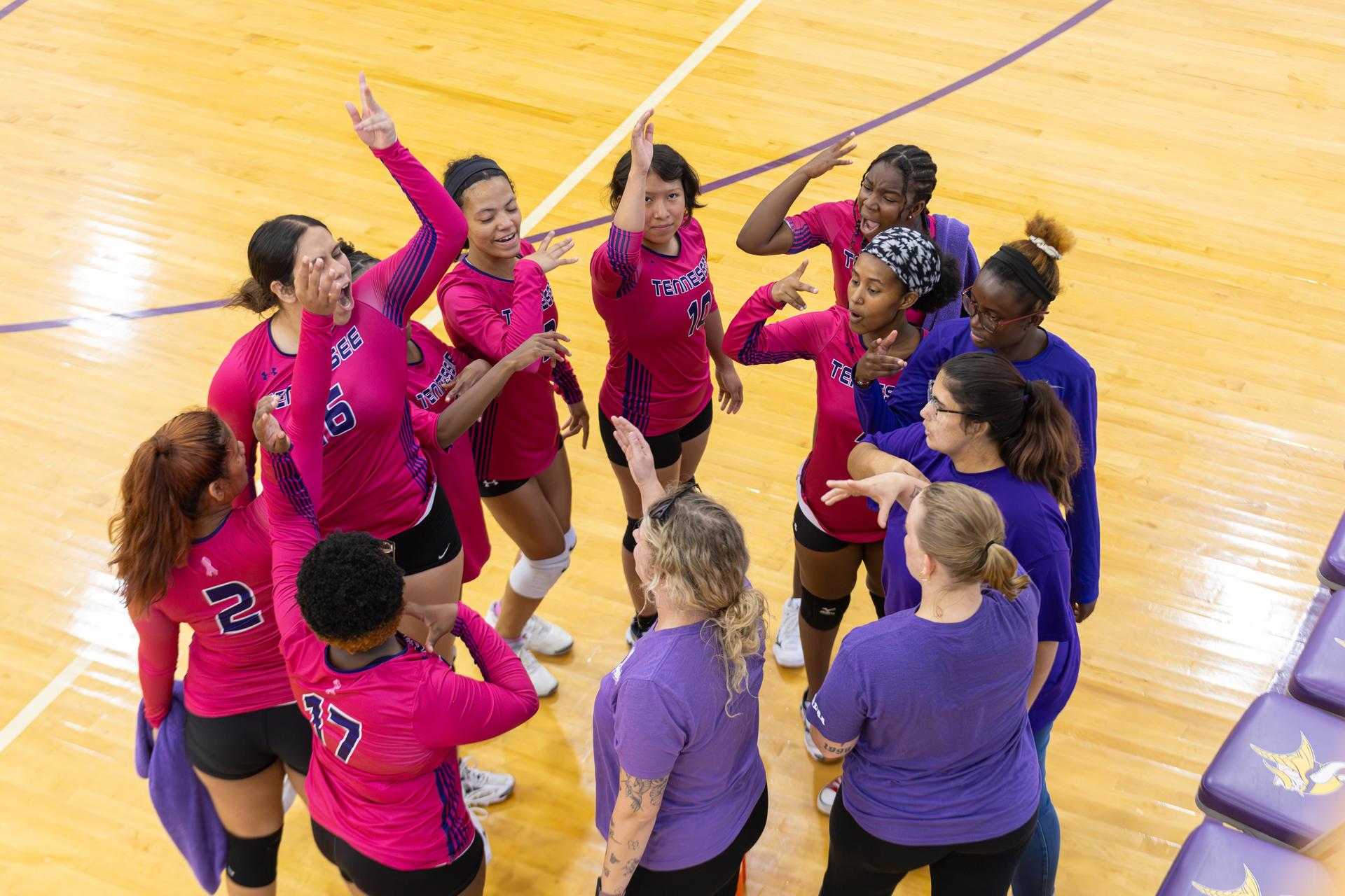 Volleyball team huddled together celebrating with enthusiastic gestures.