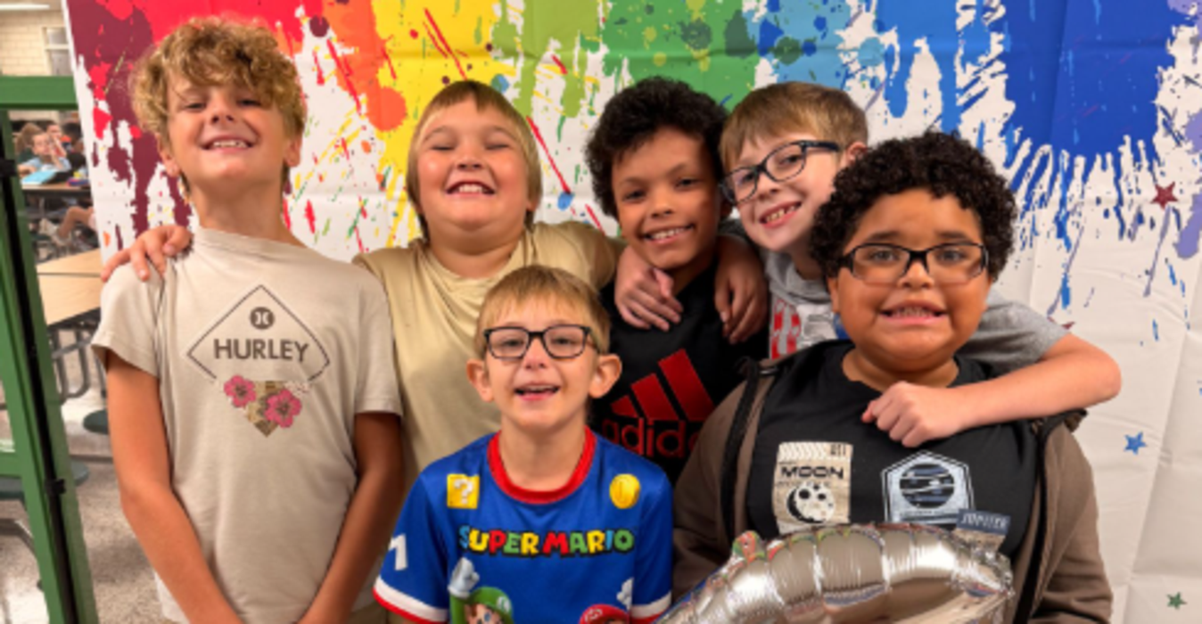 Six children posing together with a silver balloon and colorful splatter background.