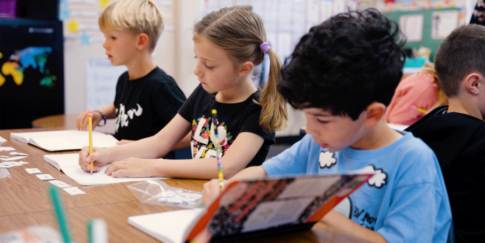 Children engage in a classroom art activity, focused on their drawing materials.