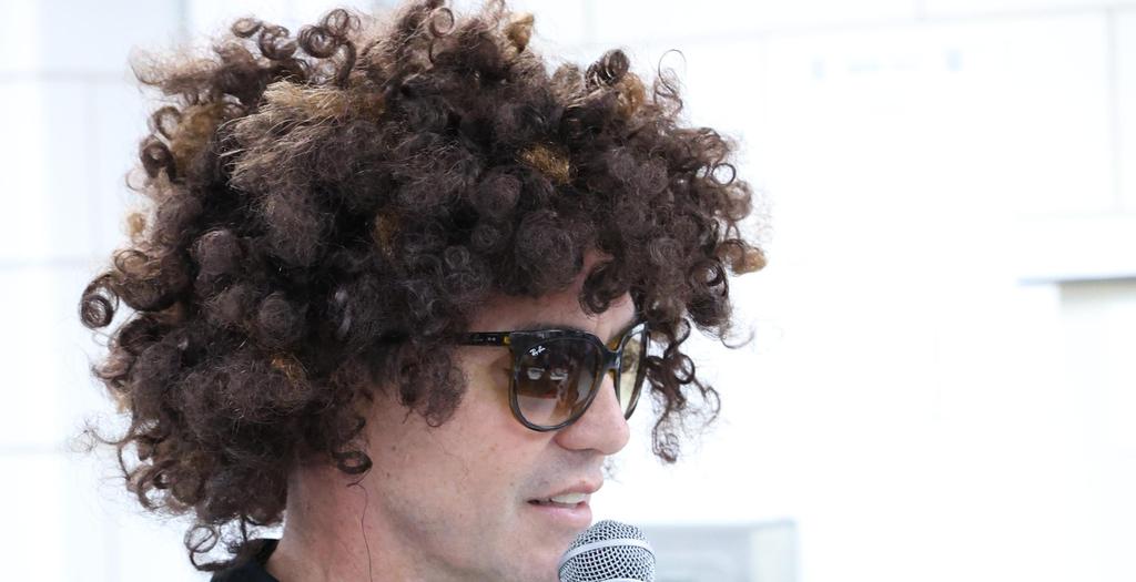 The principal, Mr. Zapata, wearing a wig and sunglasses, holding a microphone.