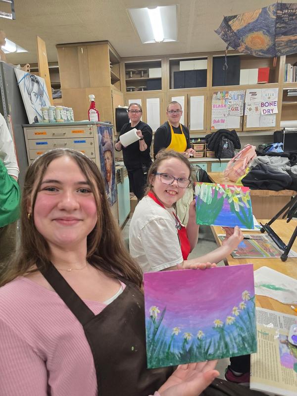 Students engaged in painting, displaying their artwork with smiles.