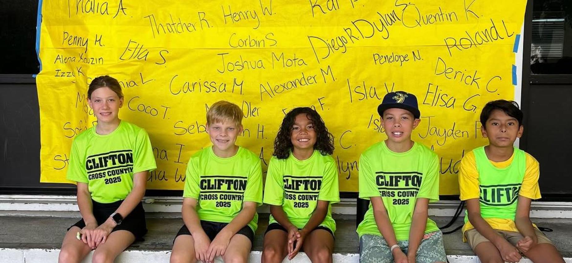 Five children in bright green shirts sitting in front of a yellow banner with names.