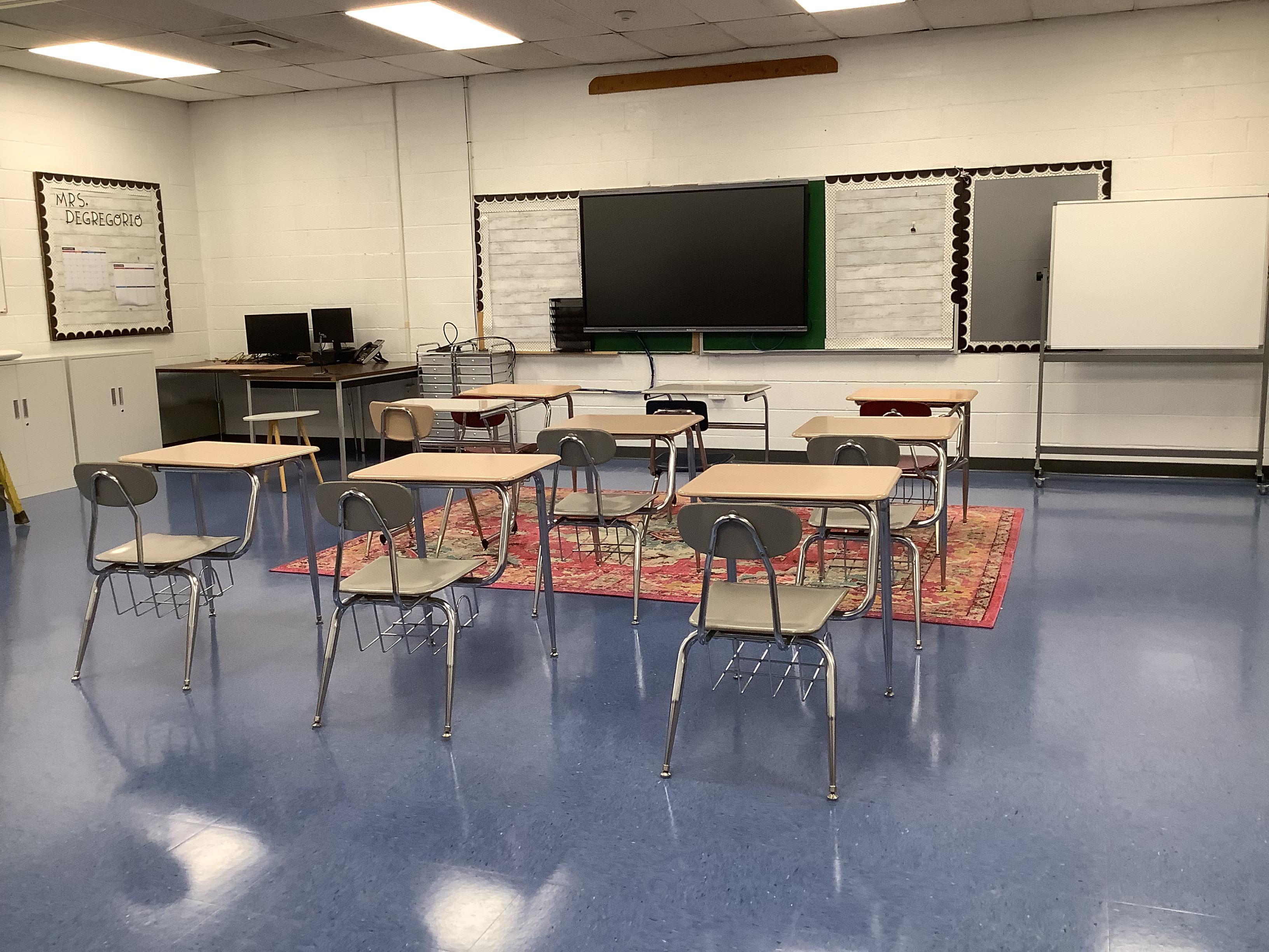 An empty classroom featuring student desks positioned around a central rug.
