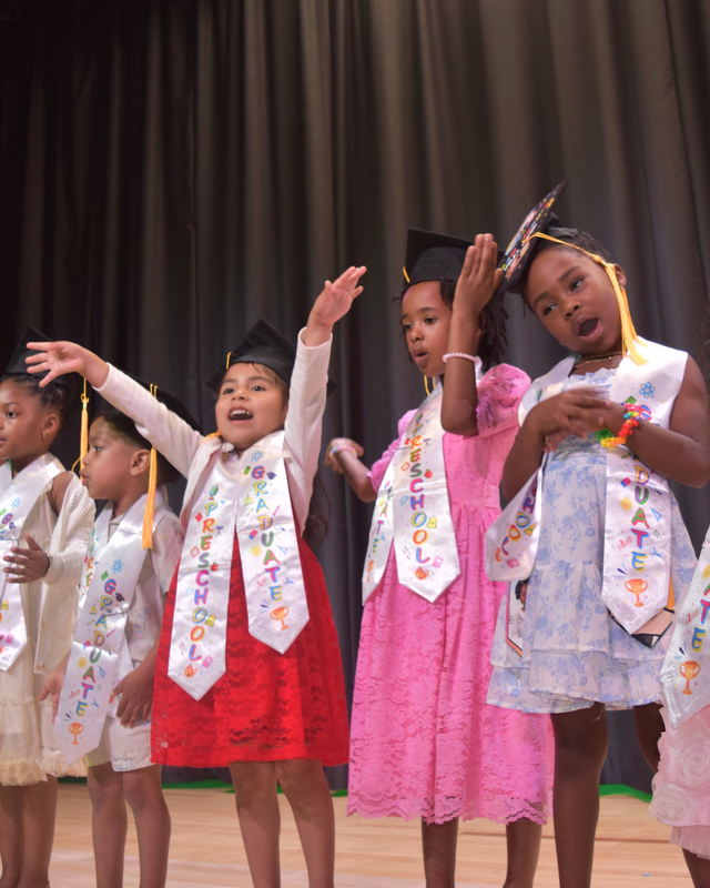 Students act out a song on stage, waving hands in air