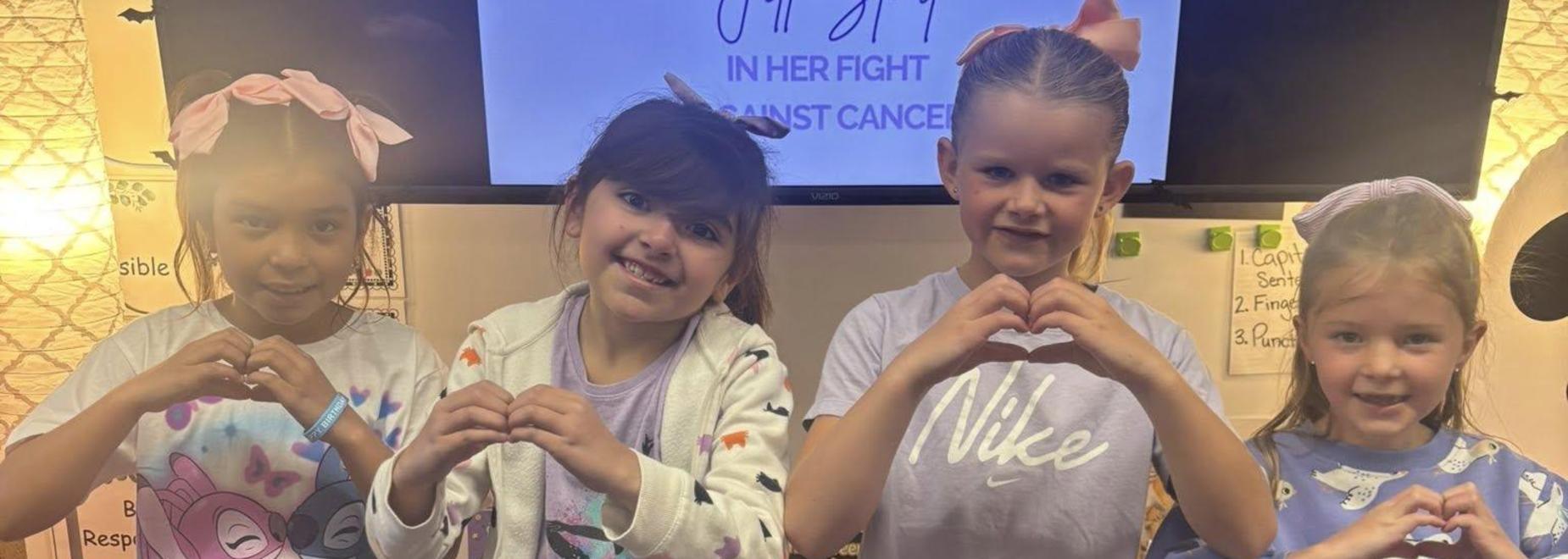 Four children making heart shapes with their hands, smiling together.