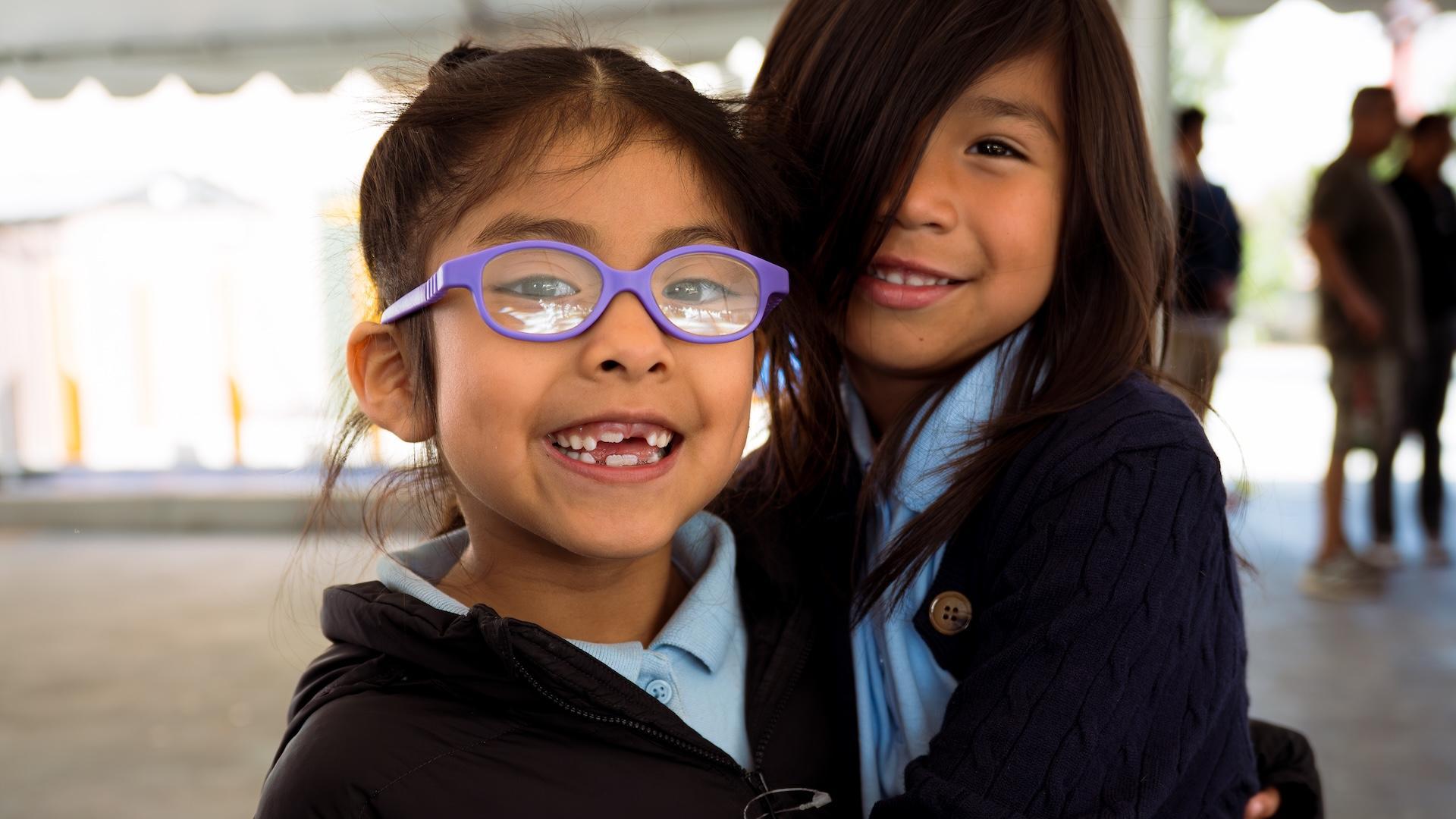 Two girls smiling and embracing each other in a casual setting.