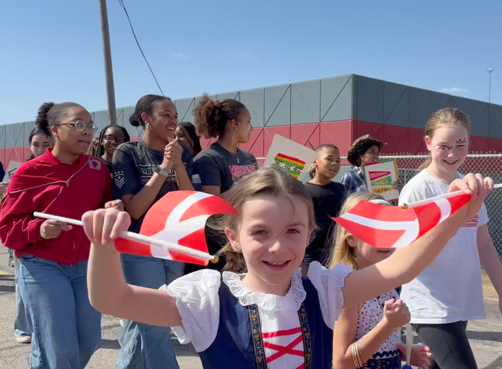 A smiling girl holds up two Danish flags in a parade 