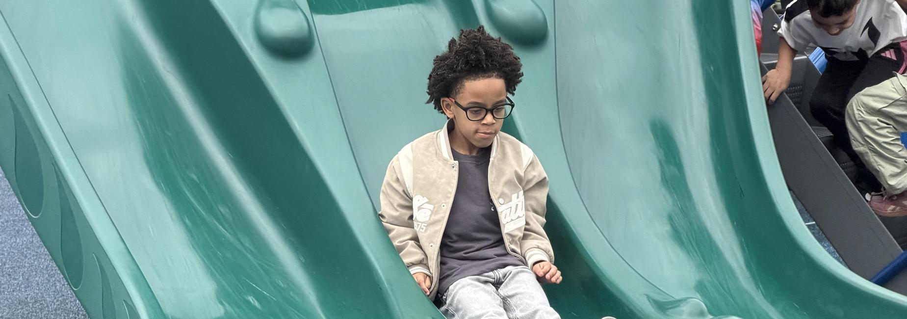 Children playing on a large green slide at a playground.