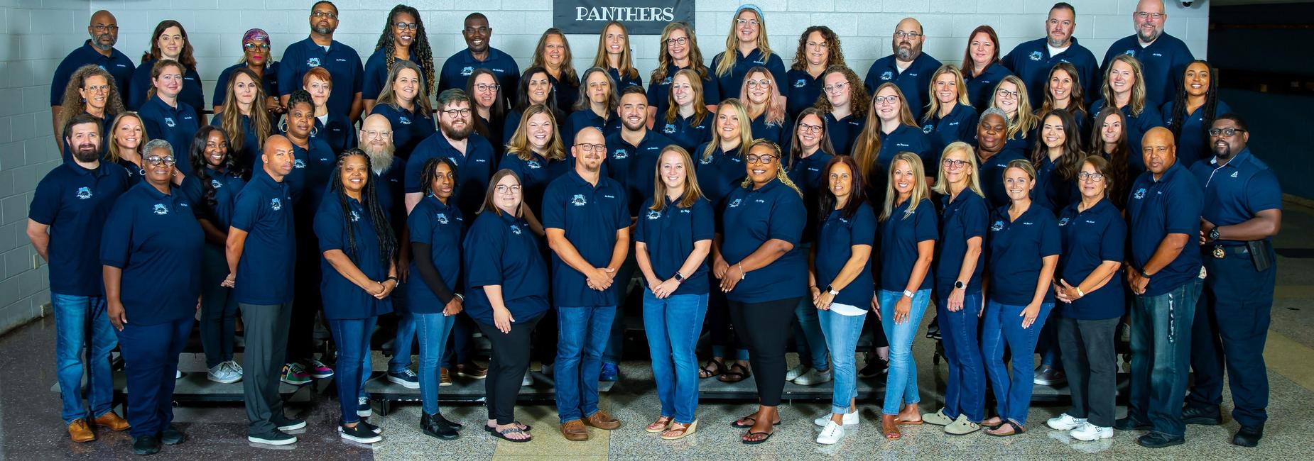 A large group of diverse individuals in matching navy blue shirts posing together cheerfully.