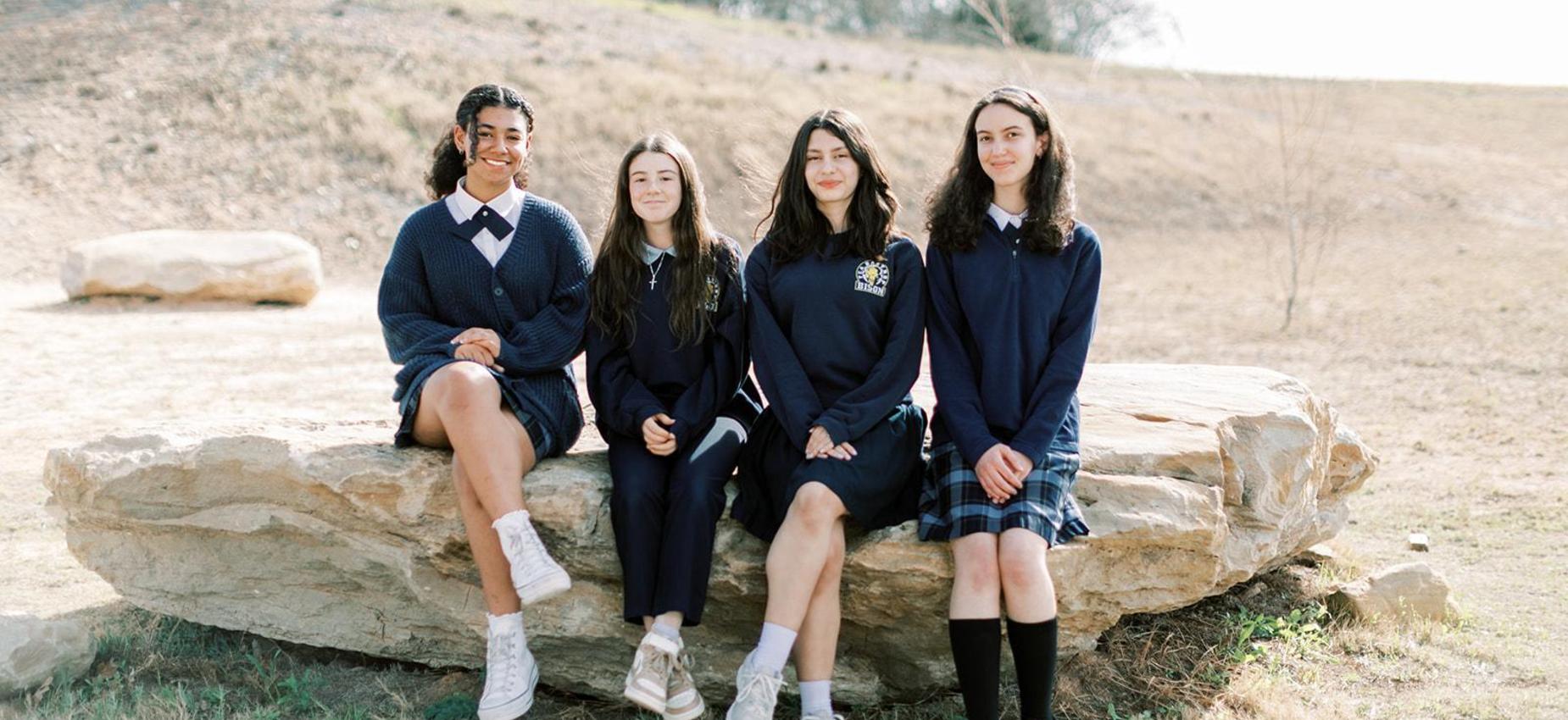 Four upper school students sit together on a rock outside