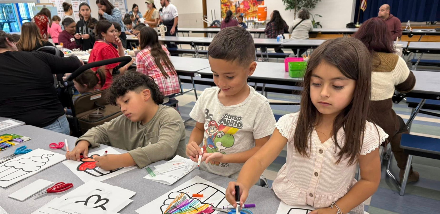 2 boys and a girl working on a coloring activity at a cafeteria table