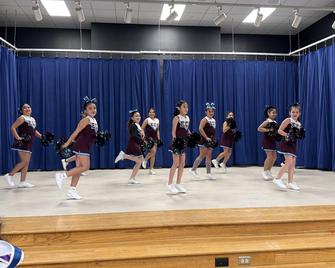 Cheerleaders dancing on stage and wearing maroon and white uniforms
