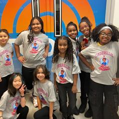 Group of children wearing matching T-shirts, smiling in front of an artistic door.