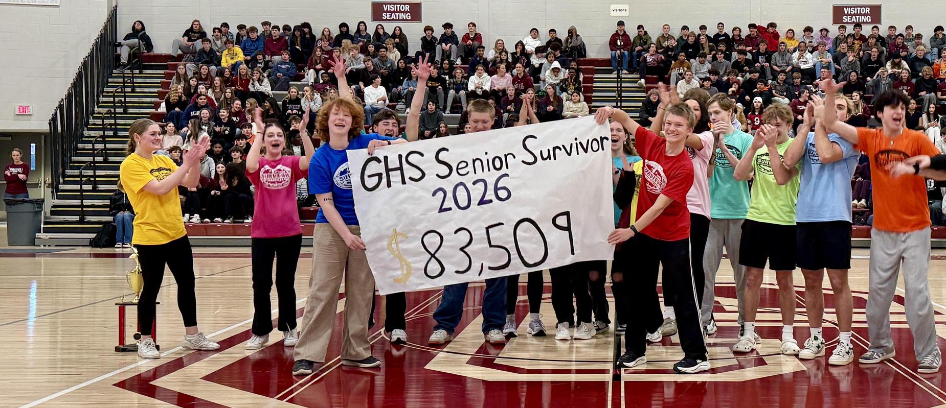 Grandville Senior Survivors hold up sign that says $83,509 and 16 seniors are clapping in the middle of the gym
