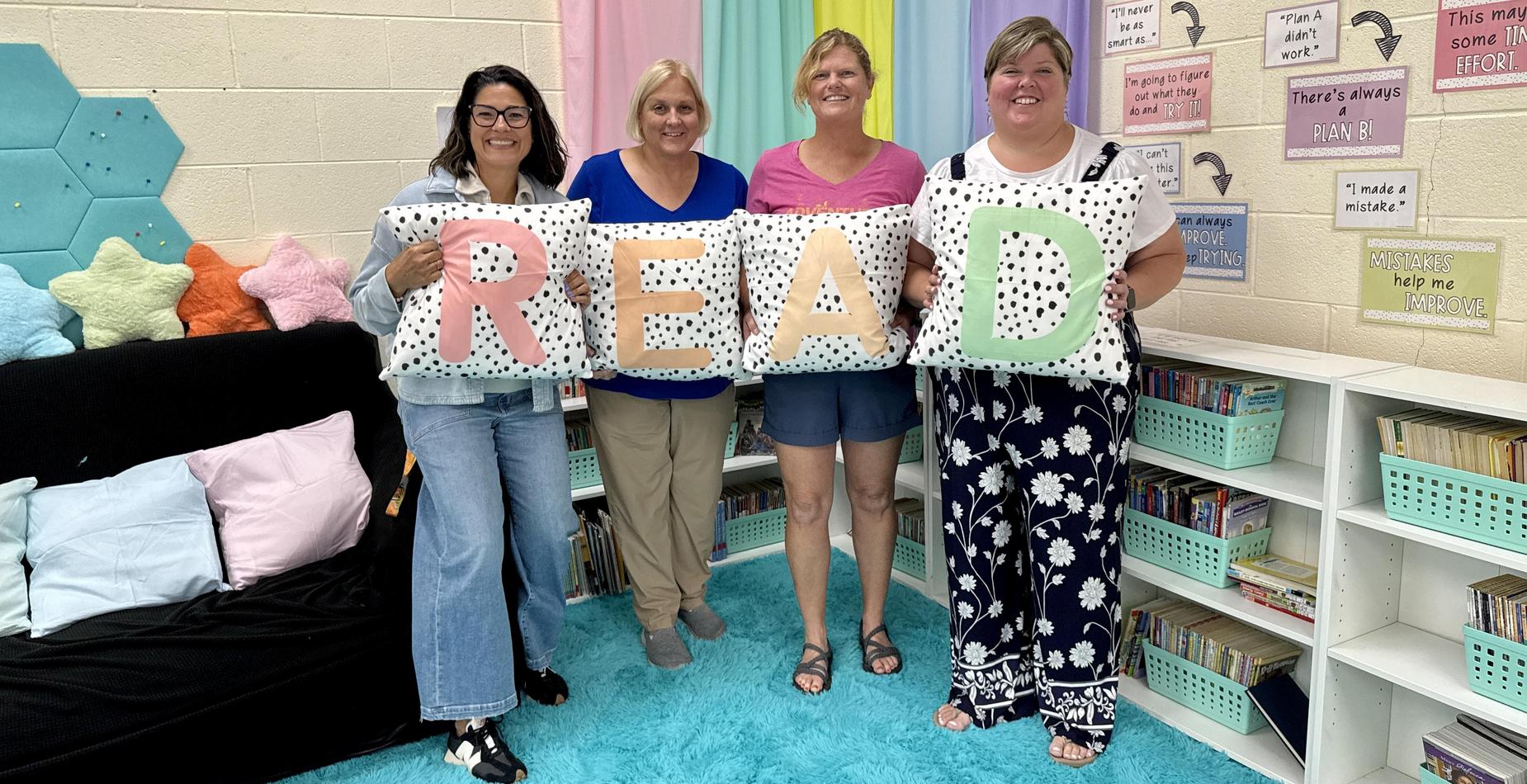 Teachers holding READ pillows in reading nook