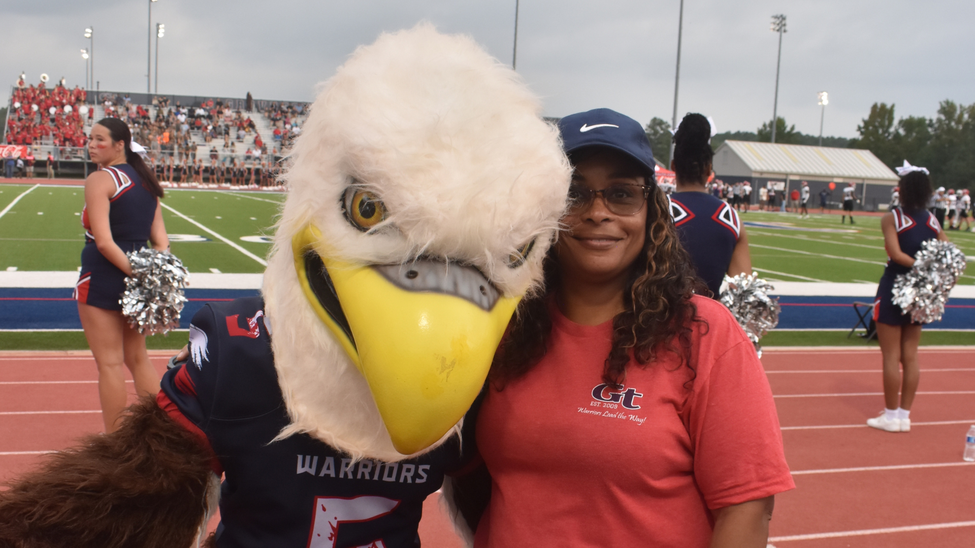 A woman poses with a large eagle mascot at a sports event on a field.