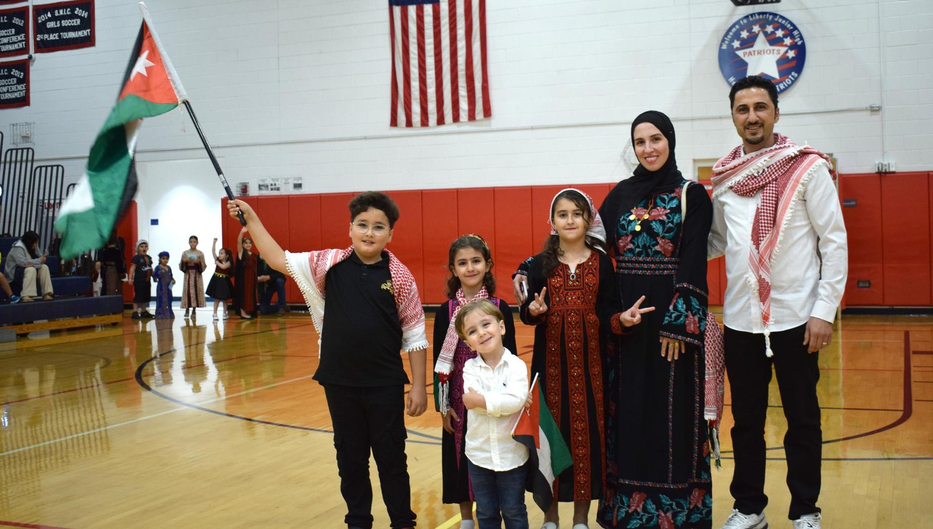 A family in traditional clothing holding a Jordanian flag, posed in a gymnasium.