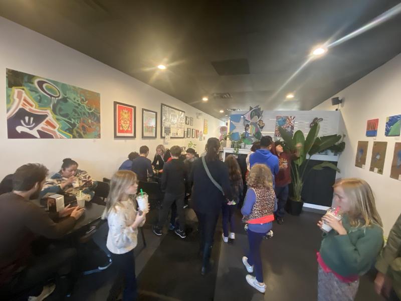 A lively café scene with diverse patrons chatting and enjoying refreshments in a colorful artistic space.