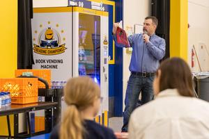 Chris holds a book and reads to the students