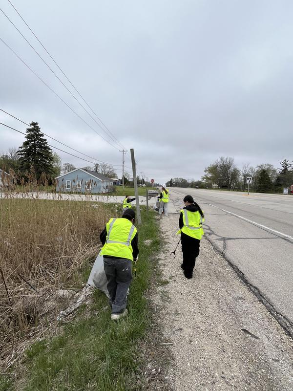 Volunteers walking along a roadside while collecting trash in bags.