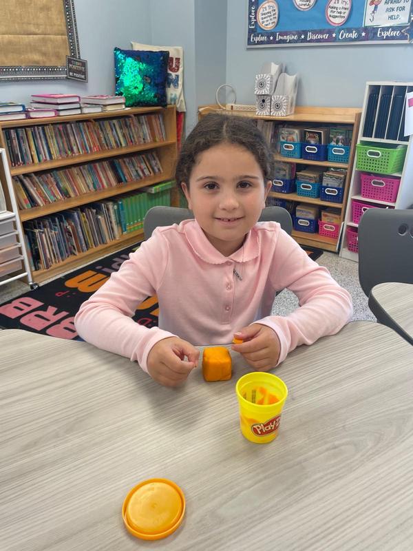 A third grade girl sculpts with playdough.