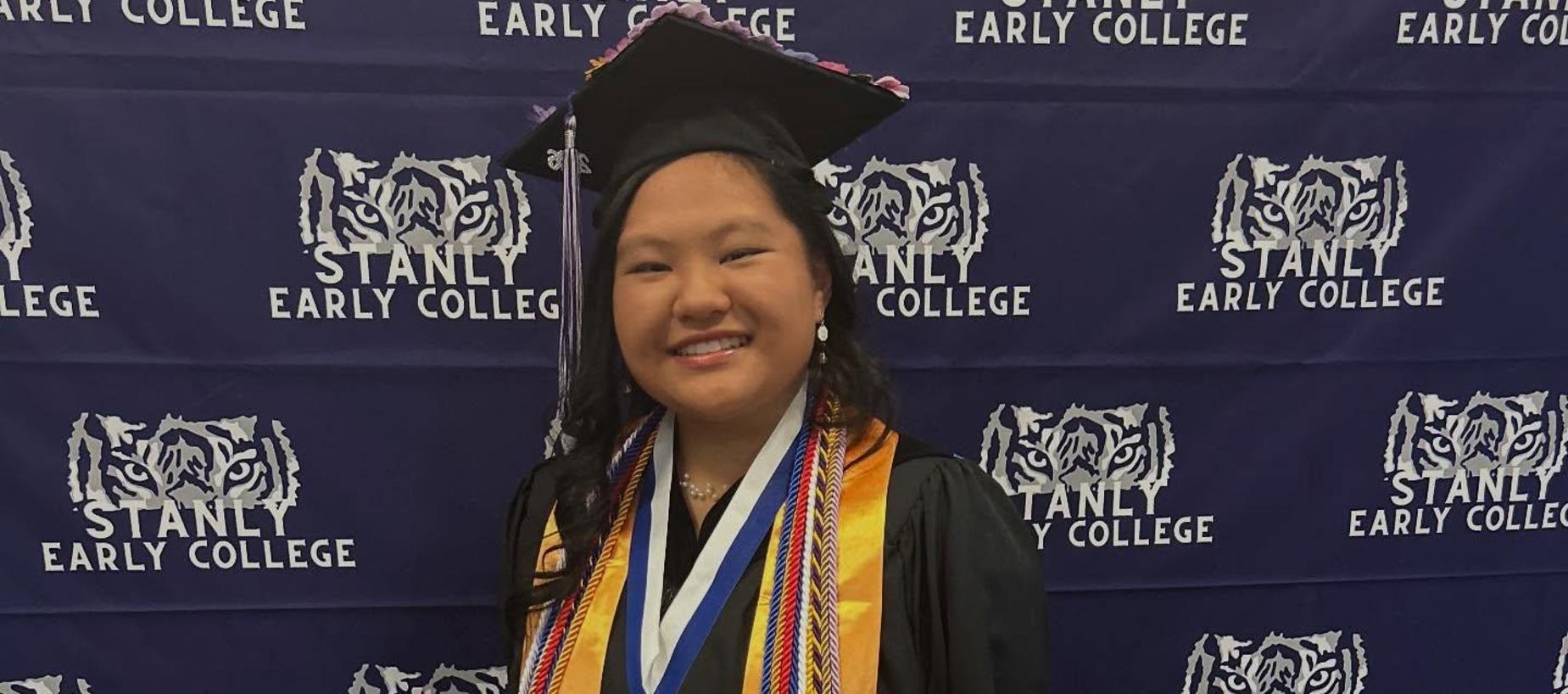 Student in graduation attire poses with medals and stoles against a school backdrop.