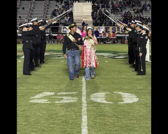 A couple walks down a football field under an arch of raised flags.