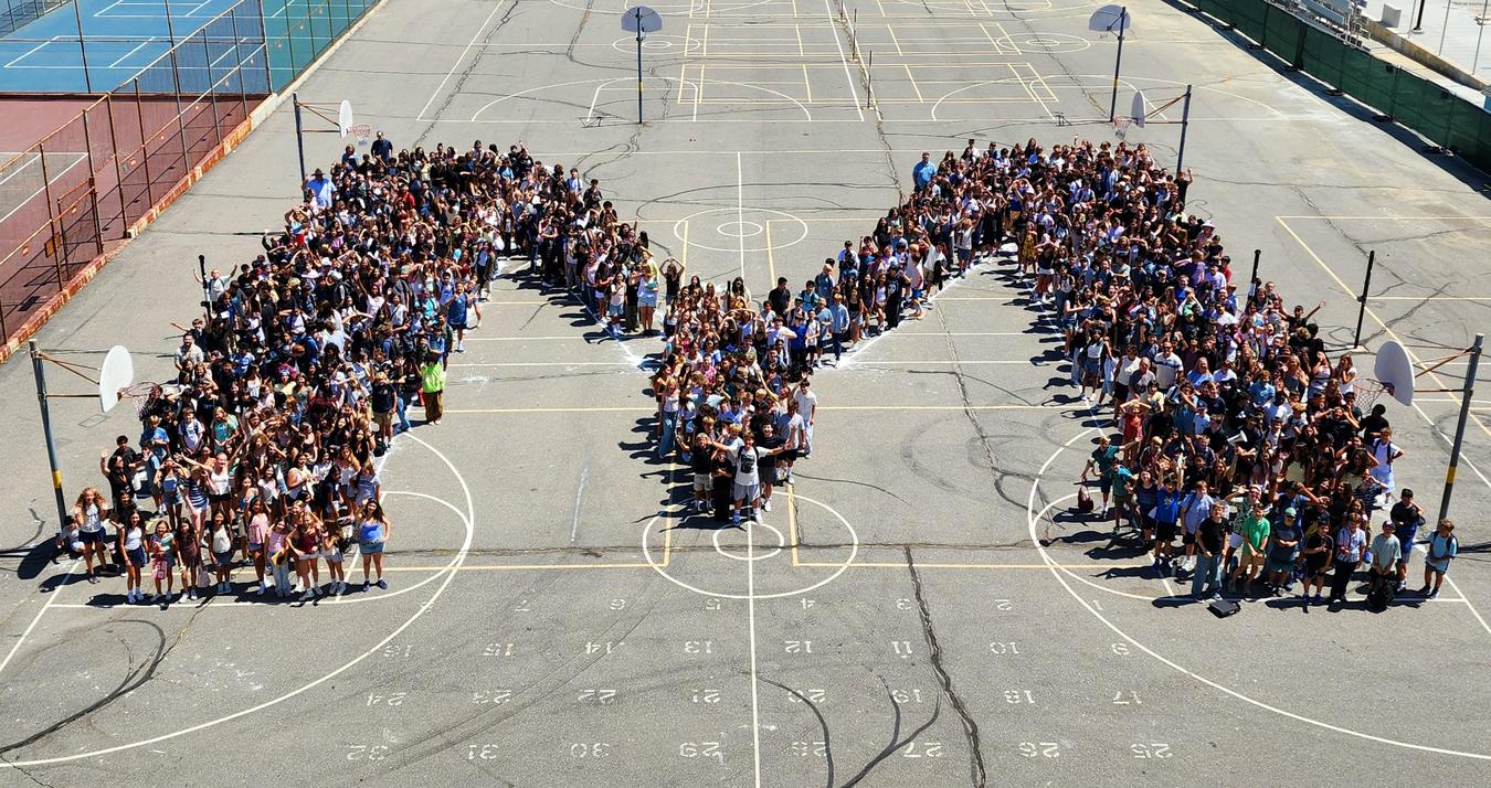 A large group of people forming the letter 'M' on a basketball court.
