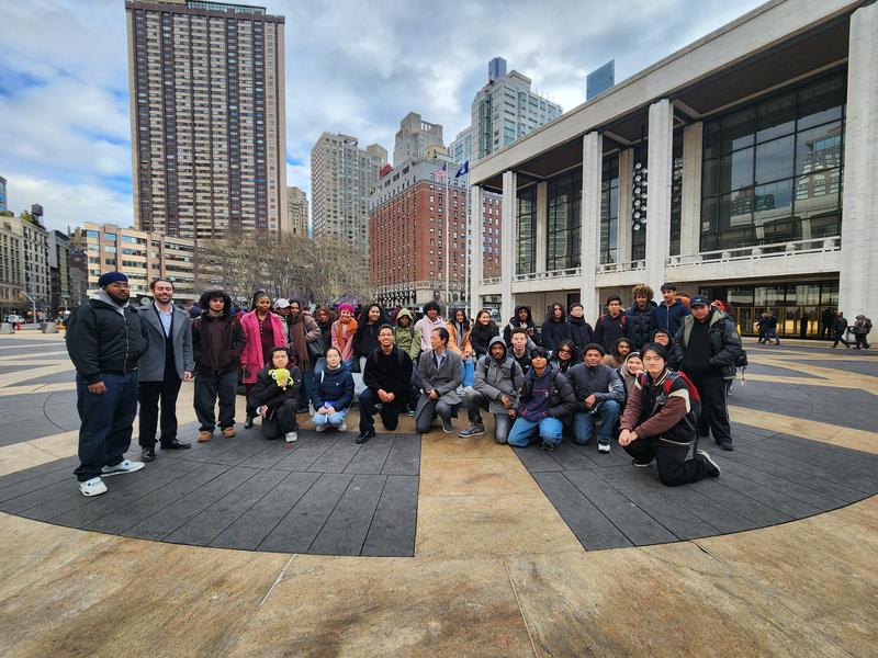 A large group of people gathered in front of a cultural building in a city square.
