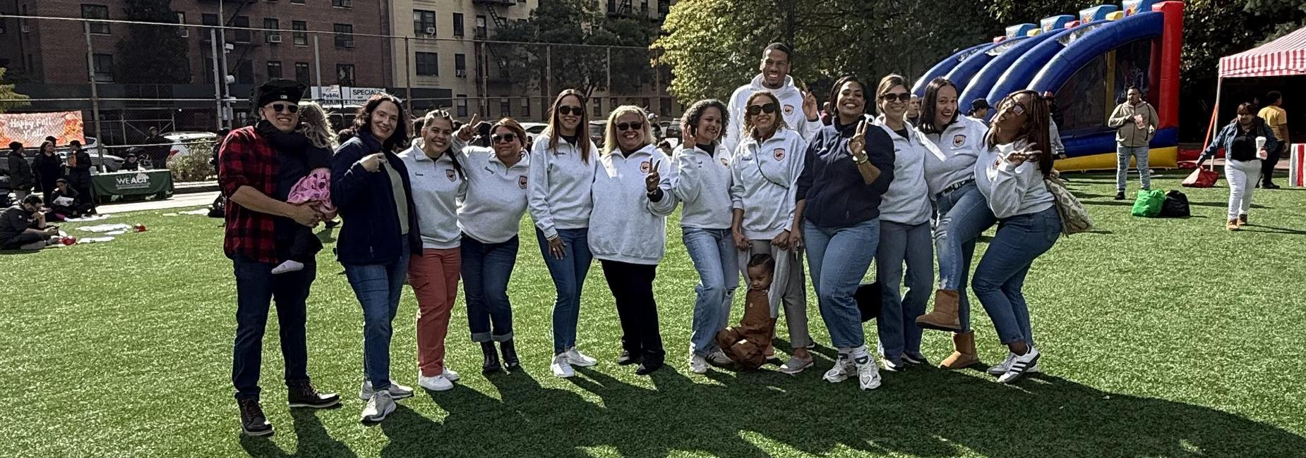 Group of people posing outdoors on a grassy field at a community event.