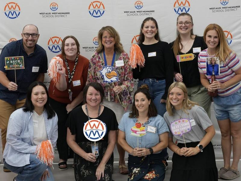 Group of diverse adults posing for a photo at a school district event, holding props.