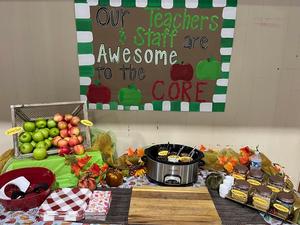 A colorful display of fall-themed decorations, food, and apples with a supportive sign.