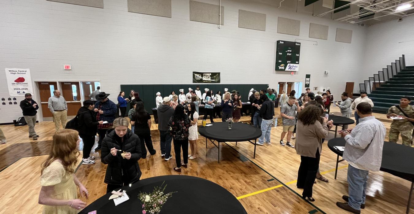 A large group of people mingling at a gathering in a gymnasium.