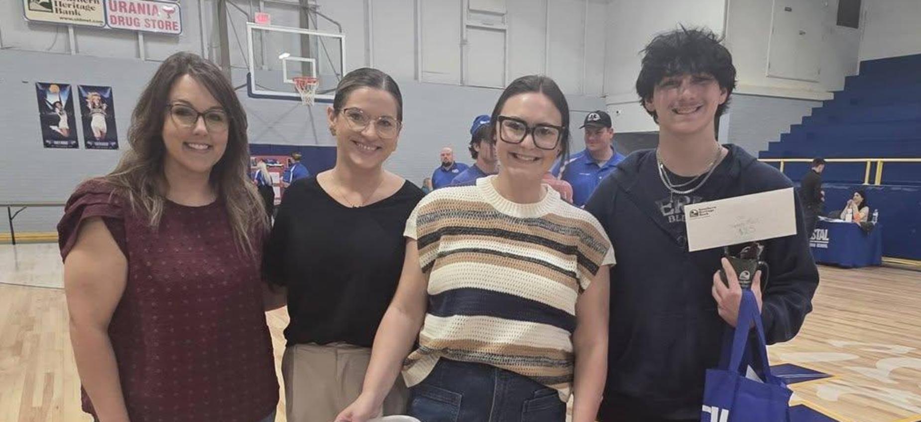 Four adults standing together, smiling and holding a basket at an event.