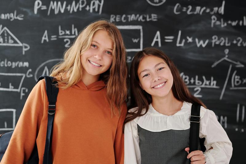 Two smiling students in front of a blackboard with math equations