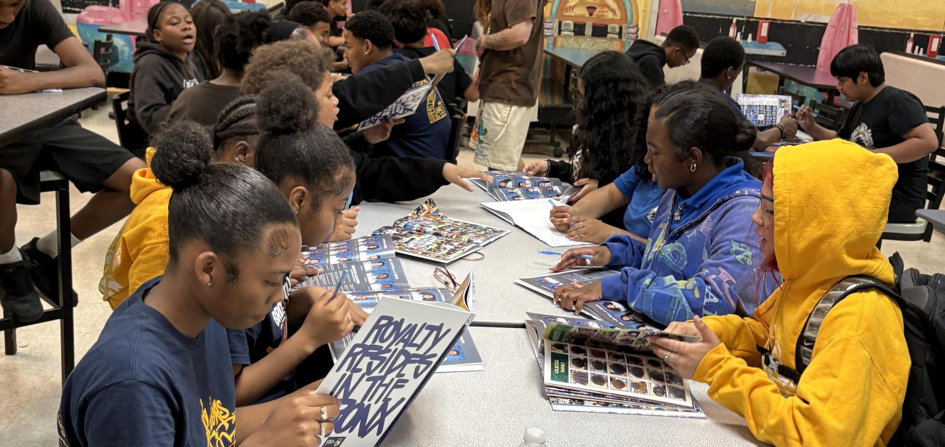 Students sitting in lunchroom with yearbooks on the table for Yearbook Signing Day
