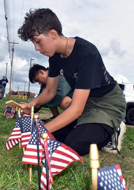A teen carefully arranging small American flags in grass.
