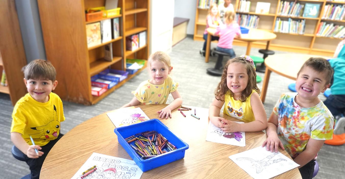 Four students color at a library table.