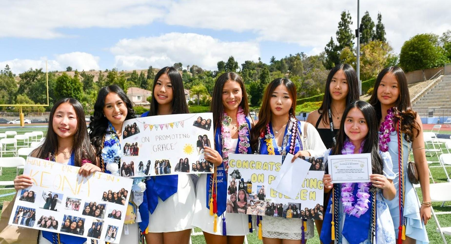 Group of graduates holding posters and certificates, celebrating on a field.