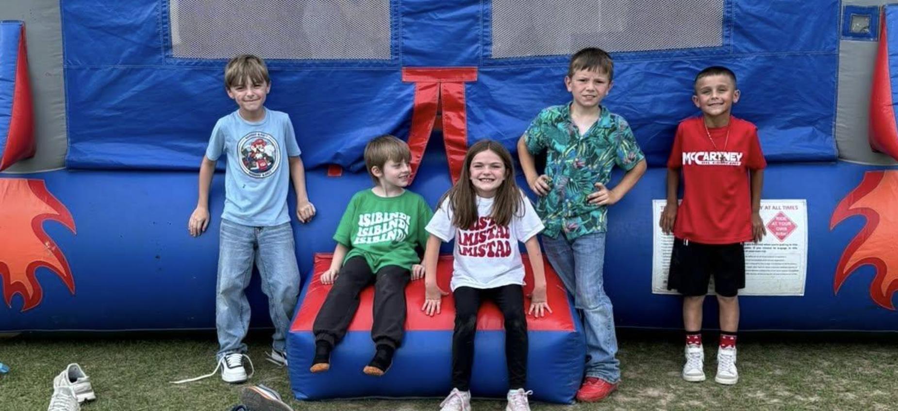Six kids sitting on a blue bounce house with playful attire.