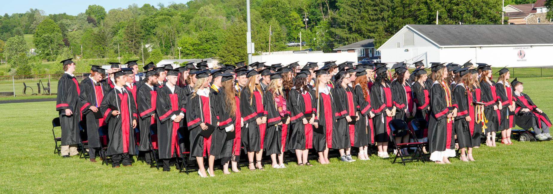 A graduation ceremony with students wearing caps and gowns outdoors.