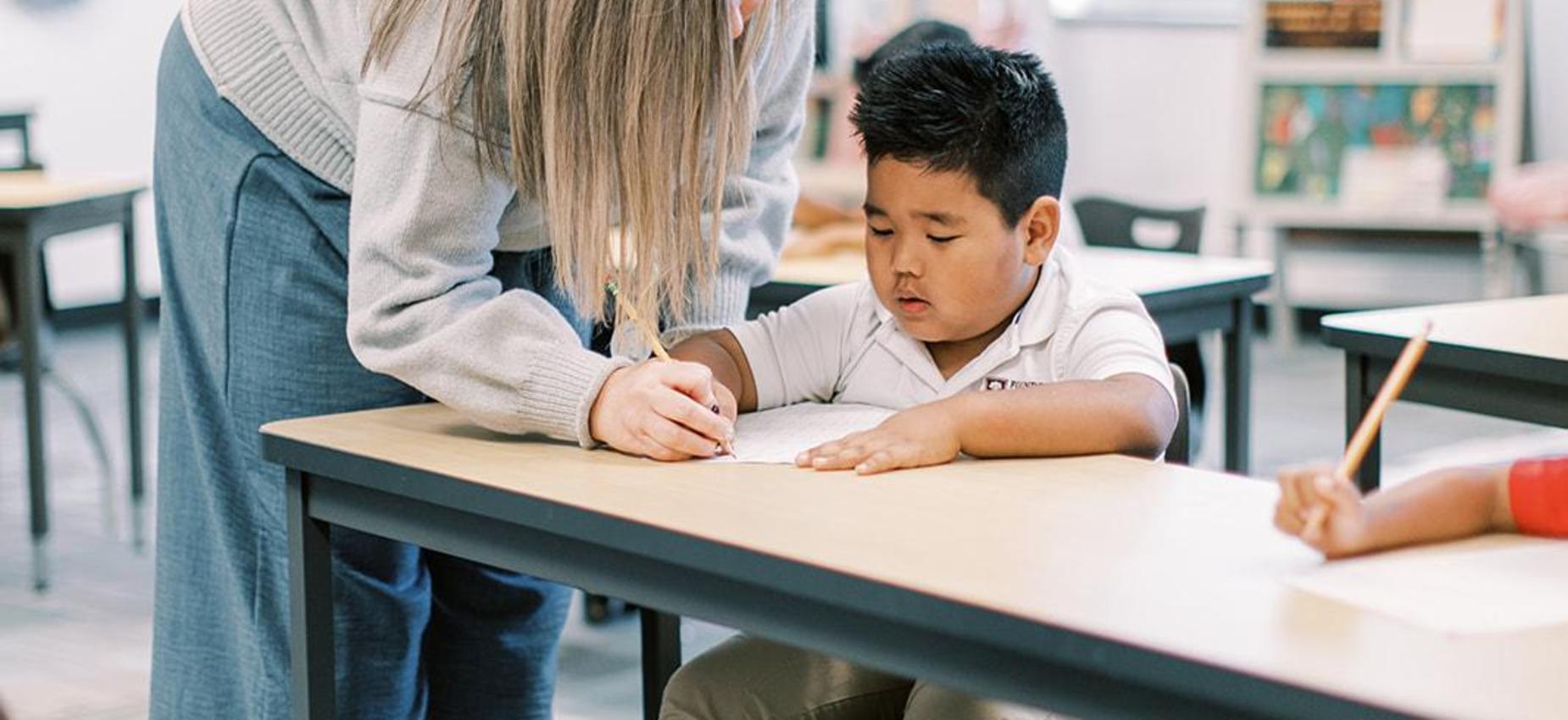 Teacher leaning over to help a student with his work at his desk