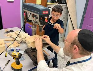 A student looks on as Rabbi Rubin sets him up to complete his box.