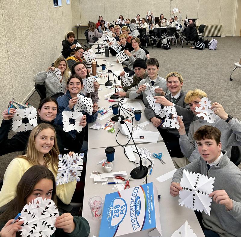 Group of students making snowflakes at a long table in a classroom.