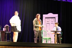 one seated at table talking to another man standing with a girl smiling off in the background