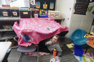 Girls build a fort using blankets and chairs.
